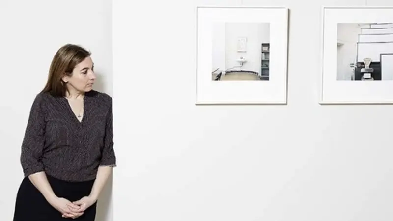 Eine Frau blickt seitlich auf Fotografien, die an einer weißen Wand hängen.